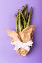 Directly above view of asparagus bunch in brown paper tied with white ribbon on purple background Royalty Free Stock Photo