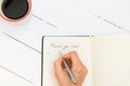 Directly above view of woman`s hand writing in a gratitude journal thank you list with coffee mug