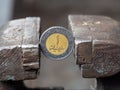 Dirham coin clamped in a metal vise. Currency and United Arab Emirates economy under the onslaught
