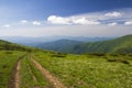 Dirt car track on green grassy hill leading to woody mountains ridge on bright blue sky copy space background. Tourism and Royalty Free Stock Photo