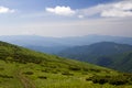 Dirt car track on green grassy hill leading to woody mountains ridge on bright blue sky copy space background. Tourism and Royalty Free Stock Photo