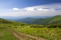 Dirt car track on green grassy hill leading to woody mountains ridge on bright blue sky copy space background. Tourism and Royalty Free Stock Photo