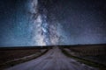 A dirt country road leads to the stars of the galaxy in a midnight night time landscape