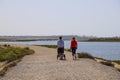 A dirt footpath with a man and a women with a baby stroller walking and gorgeous rippling blue ocean water