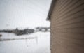 Focus on a dirty residential windo overlooking the side of a house and snow covered area