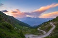 Dirt mountain road leading to high mountain pass in Italy Colle delle Finestre. Expasive view at sunset, colorful dramatic sky,