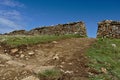 Dirt path leading up to a hole in a drystone wall with clear blue sky in the background