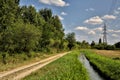 Dirt path next to a stream of water and an open space with a row of cypresses on it on a clear day Royalty Free Stock Photo