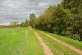 Dirt road along a meadow on a cloudy day in the Flemish countryside Royalty Free Stock Photo