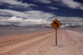 Dirt road into endlessness of Atacama desert - yellow traffic sign showing left direction, Chile