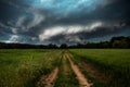 Dirt road through green field and dark stormy sky with clouds Royalty Free Stock Photo