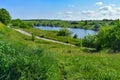 Dirt road among green hills on the shore of a pond with blue water. Bright natural panorama with a lake in the middle of juicy Royalty Free Stock Photo