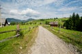 Dirt road in a green village under blue sky and white clouds Royalty Free Stock Photo