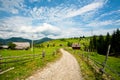 Dirt road in a green village under blue sky and white clouds Royalty Free Stock Photo