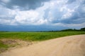 A dirt road leading into fields under a pre-storm cloudy sky. Royalty Free Stock Photo