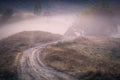 Dirt road leading to some small barn houses in a foggy dreamy landscape