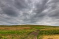 Dirt road leading to the top of a green hill at summertime, gathering storm clouds Royalty Free Stock Photo