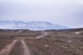 Dirt road through mountain steppe to snowy mountains in early spring in Kazakhstan Royalty Free Stock Photo