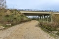 A dirt road passing under a highway bridge with two independent carriageways with circular concrete pillars Royalty Free Stock Photo