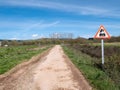 Dirt road and stones surrounded by vegetation, crop fields and a vertical sign indicating train danger due to the proximity of a l Royalty Free Stock Photo