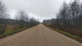 A dirt road with traces of car tires passes among the fields. Grass and trees grow along the sides of the road. A power line runs Royalty Free Stock Photo