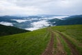 Clouds over valley mountain landscape and dirt road tracks on the green meadow Royalty Free Stock Photo