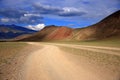 Dirt road winds at the foot of the red mountains under the thunderclouds in the sky. Siberia Royalty Free Stock Photo