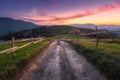 Dirt road, wooden fence, green hills in mountain valley at sunset
