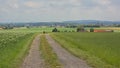 Dirtroad with lone hiker thorugh a flemish landscape with farmland and hills with forest