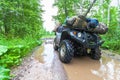 The dirty ATV stands with bags and stuff in the deep muddy puddle on the forest road