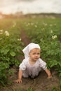 A dirty child is playing in the mud. A girl crawls in a field of blooming potatoes.