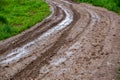 Dirty clay mud road turn with puddles and tire tracks - closeup with selective focus and linear perspective