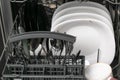 Dirty dishes in dishwasher. White plates, spoons and fork, glasses and cups after eating before washing. Royalty Free Stock Photo