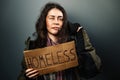 A dirty disheveled woman holds a cardboard sign with the text homeless. Dark background. The concept of helping the Royalty Free Stock Photo