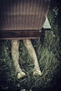 Dirty female legs sticking out from under an armchair in a field, dark mood unusual concept