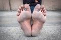 Dirty foot of a man sitting on concrete floor.