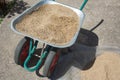 Dirty green wheelbarrow full of sand. Handcart standing in the construction site or household
