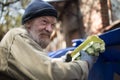 Dirty homeless man holding packing for eggs, standing by the trash can. Royalty Free Stock Photo