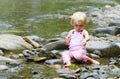 Dirty little girl in a pink suit sitting on the rocks in the river