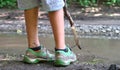 Dirty and mosquitoes bitten legs of caucasian child standing next to the muddy puddle with wood branch as a pole in hands