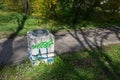 Concrete trash can with scribbles graffiti in green grass in park.