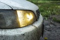 Dirty and muddy headlights on the car during slush and rainy weather on the asphalt