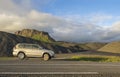 Dirty off road car standing next asphalt road with Iceland northern summer landscape, green eroded mountains and blue sky, white c