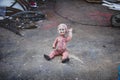 Dirty plastic baby doll sitting on the ground in front of a metal shop waving