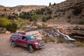 Red pickup camping rig on rocky trail near waterfall in southern