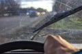 Dirty scratched car windshield with wiper through blurred steering wheel with driver`s hand on blurred background