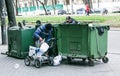 Dirty tramps search for food and used PET bottles in a trash bin on the street. Homeless men
