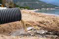Dirty water pours down from grey plastic sewer drain pipe on empty sandy sea beach near tranquil bay on summer day Royalty Free Stock Photo