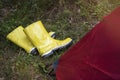 Dirty yellow rubber boots with a white border lie on the wet grass near the tent in a tourist camp