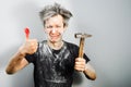 Dirty young builder guy in plaster is hold a hammer and sick finger from blow on a gray background at home during repairs